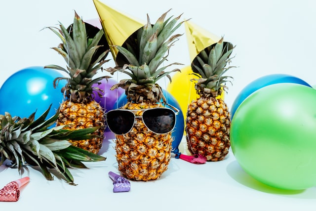 trzy ananasy w czapeczkach imprezowych, kolorowe balony