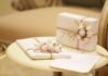 dwa prezenty zapakowane w jasny papier, przewiązane brązową wstążką i ozdobione różowymi kwiatami