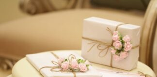 dwa prezenty zapakowane w jasny papier, przewiązane brązową wstążką i ozdobione różowymi kwiatami